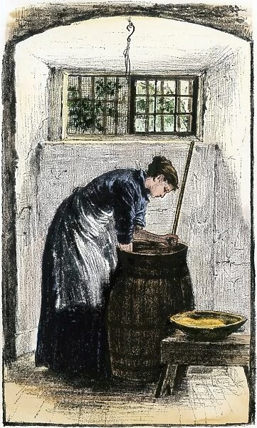 Churning butter. Woman bending over a churn to gather butter.
